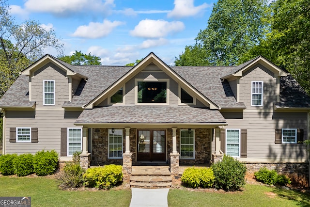 view of front of house with stone siding, covered porch, and roof with shingles