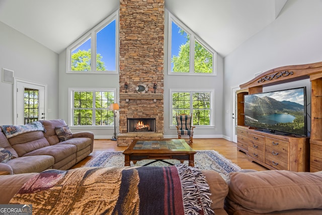 living area featuring a stone fireplace, a wealth of natural light, light wood finished floors, and high vaulted ceiling