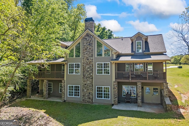 rear view of house with stone siding, a chimney, a patio area, a lawn, and a shingled roof