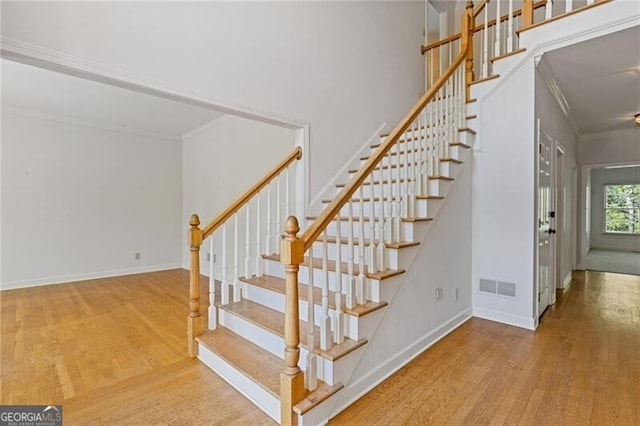 stairs featuring visible vents, baseboards, wood finished floors, and crown molding