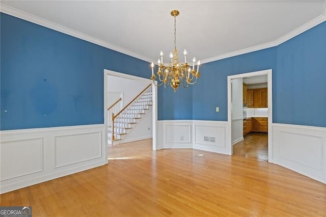 unfurnished dining area featuring wainscoting, visible vents, a chandelier, wood finished floors, and stairway