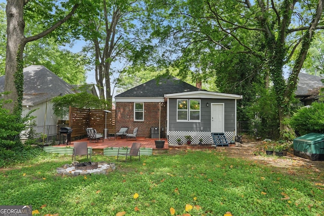 rear view of house with a lawn, a fire pit, fence, and a deck
