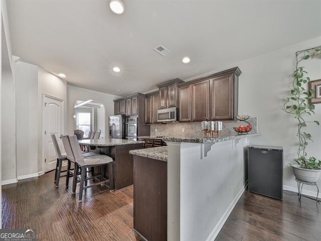 kitchen with arched walkways, visible vents, backsplash, a breakfast bar, and appliances with stainless steel finishes