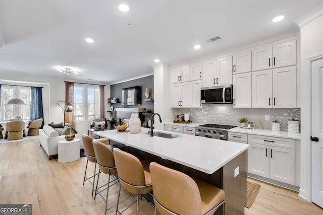 kitchen with a sink, open floor plan, visible vents, decorative backsplash, and appliances with stainless steel finishes