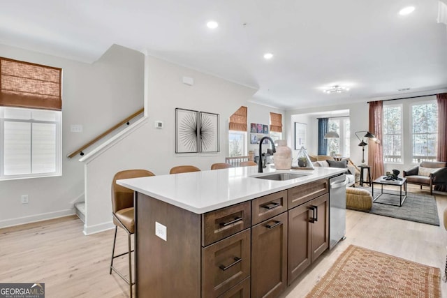 kitchen featuring light wood finished floors, a sink, open floor plan, a kitchen bar, and dishwasher