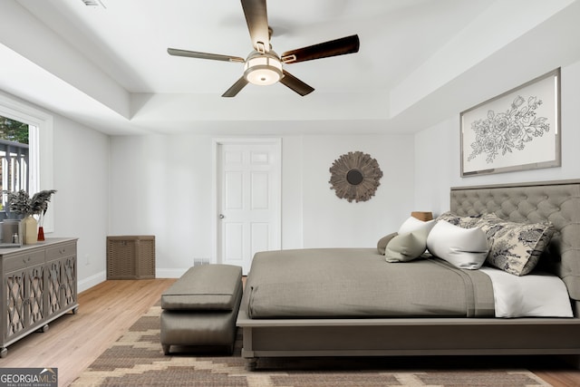 bedroom featuring baseboards, wood finished floors, and a raised ceiling