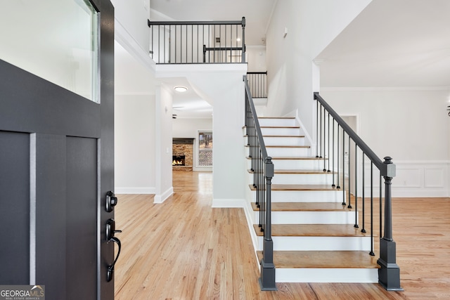 foyer entrance with stairway, a warm lit fireplace, ornamental molding, and wood finished floors