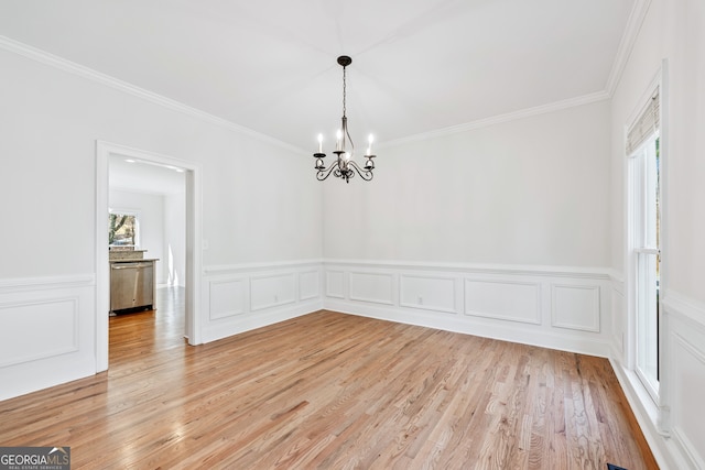unfurnished dining area with wainscoting, light wood-style floors, a notable chandelier, and crown molding