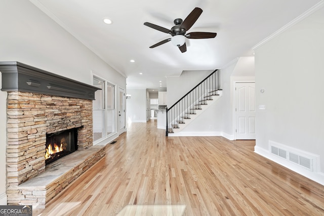 unfurnished living room featuring a stone fireplace, visible vents, baseboards, stairs, and ceiling fan