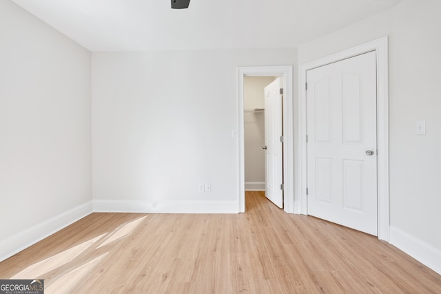 unfurnished bedroom with a spacious closet, baseboards, light wood-style floors, and a closet