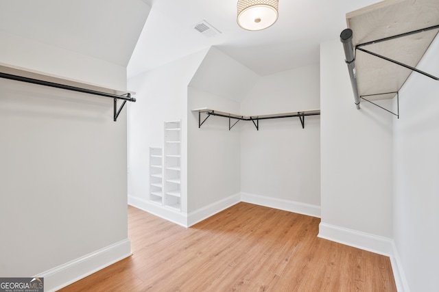 spacious closet with light wood-style floors, lofted ceiling, and visible vents