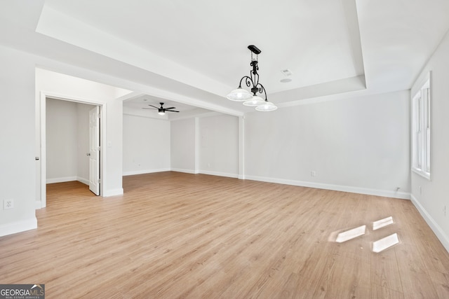 unfurnished living room featuring a raised ceiling, light wood-type flooring, a ceiling fan, and baseboards