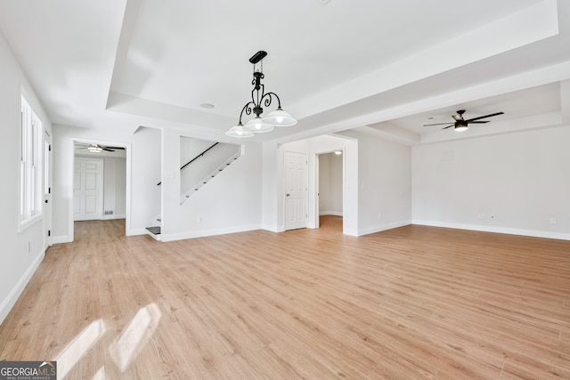 unfurnished living room with light wood-type flooring, a ceiling fan, stairway, and a raised ceiling