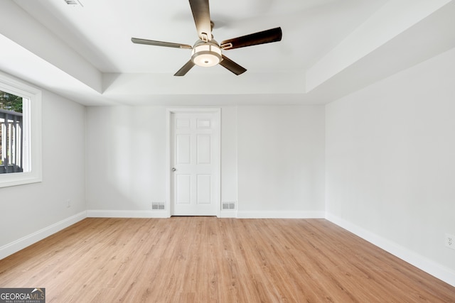 spare room with a tray ceiling, wood finished floors, visible vents, and baseboards