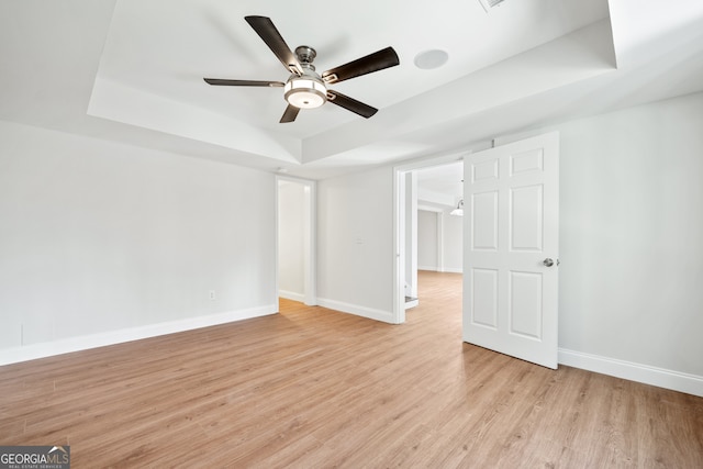 interior space featuring a raised ceiling, light wood-style floors, and baseboards