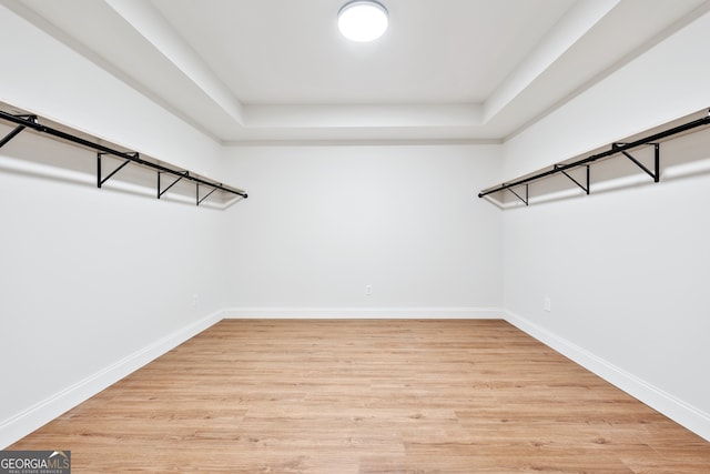 walk in closet with light wood-type flooring and a tray ceiling