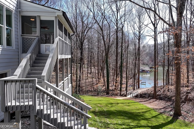 view of yard featuring ceiling fan, a sunroom, stairs, and a water view