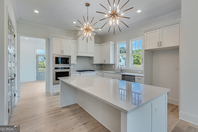 kitchen featuring white cabinets, a sink, crown molding, a chandelier, and appliances with stainless steel finishes