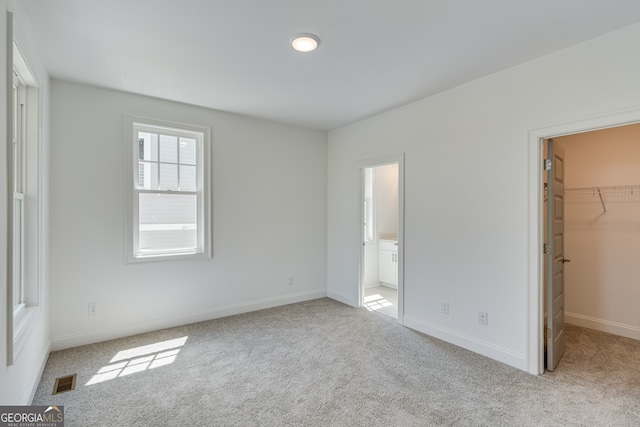 unfurnished bedroom featuring a walk in closet, carpet floors, visible vents, and baseboards