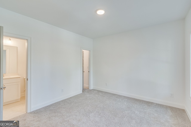 unfurnished bedroom featuring baseboards, ensuite bath, and light colored carpet