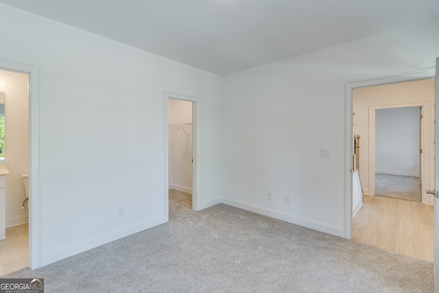 unfurnished bedroom with a walk in closet, light carpet, ensuite bath, and baseboards