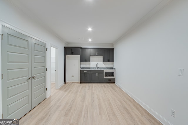 kitchen with a sink, stainless steel microwave, light wood-type flooring, baseboards, and ornamental molding