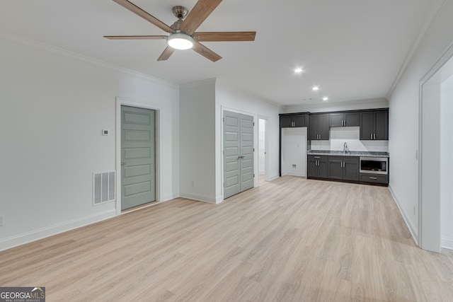 unfurnished living room featuring a ceiling fan, visible vents, a sink, and crown molding