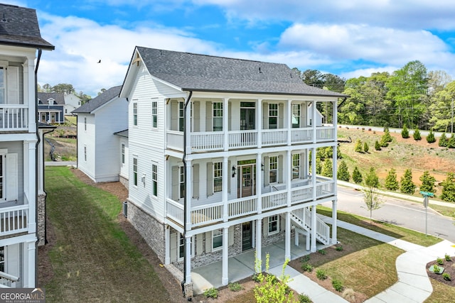 back of property featuring a porch, a patio area, a lawn, a shingled roof, and a balcony