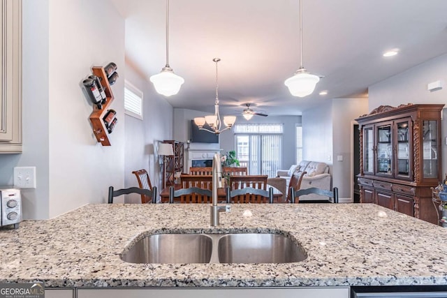 kitchen with a sink, open floor plan, light stone countertops, hanging light fixtures, and a chandelier