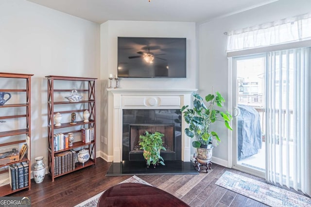 living room featuring wood finished floors, a fireplace with raised hearth, baseboards, and a ceiling fan