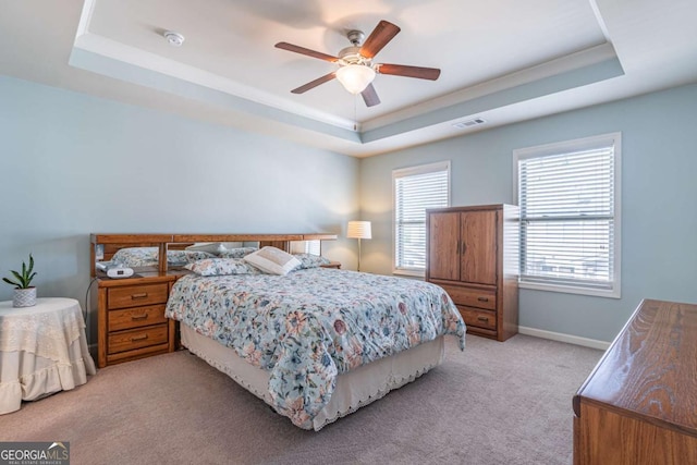 bedroom featuring a raised ceiling, light colored carpet, baseboards, and a ceiling fan
