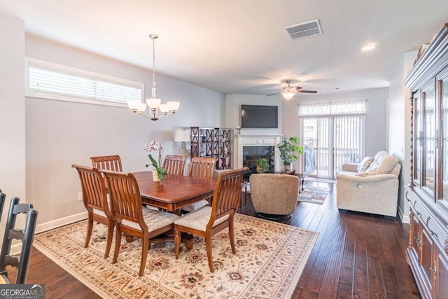 dining room with dark wood-type flooring, a ceiling fan, a chandelier, a tile fireplace, and recessed lighting
