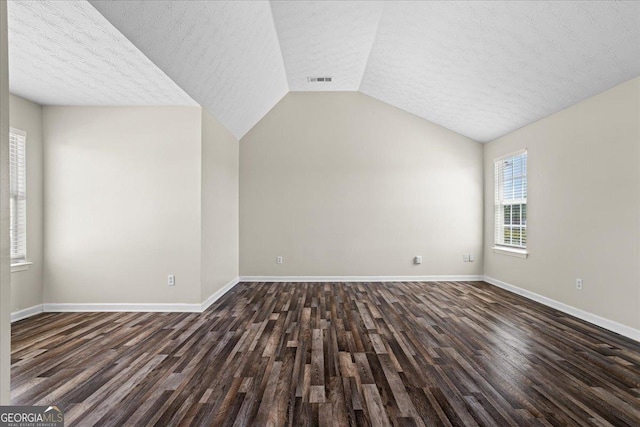 unfurnished living room with vaulted ceiling, baseboards, a textured ceiling, and dark wood-style floors