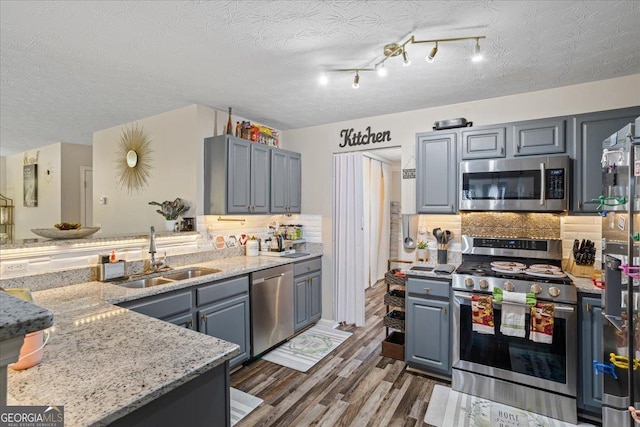 kitchen featuring wood finished floors, a textured ceiling, a sink, stainless steel appliances, and backsplash
