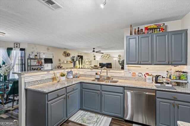 kitchen with a peninsula, stainless steel dishwasher, a sink, a textured ceiling, and open floor plan