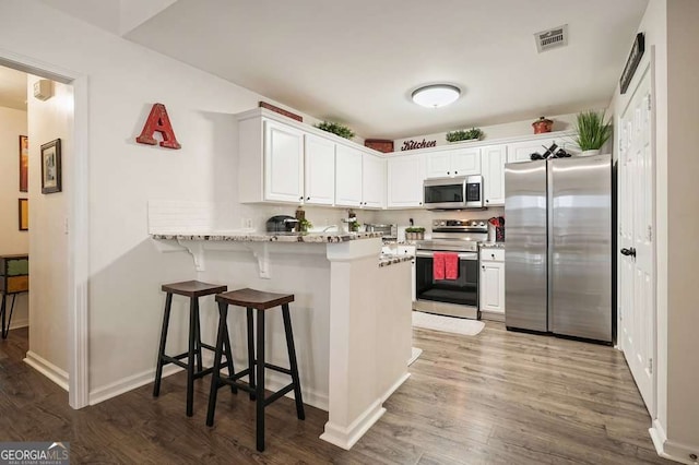 kitchen with white cabinets, a peninsula, dark wood finished floors, a breakfast bar, and appliances with stainless steel finishes