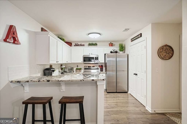 kitchen with a peninsula, a breakfast bar, white cabinetry, and appliances with stainless steel finishes