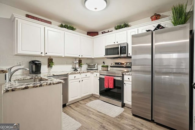 kitchen featuring white cabinets, light wood finished floors, a sink, light stone countertops, and appliances with stainless steel finishes