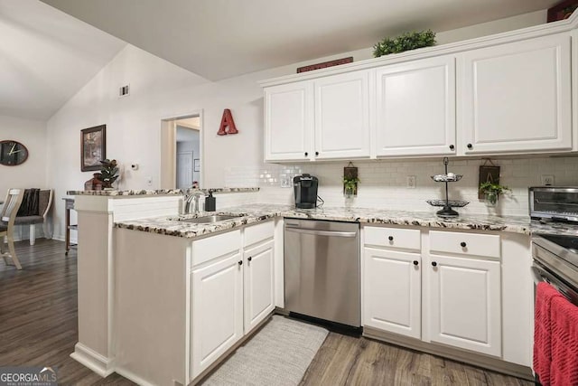 kitchen with vaulted ceiling, stainless steel dishwasher, a sink, a peninsula, and tasteful backsplash
