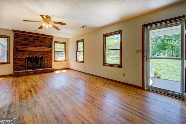 unfurnished living room with ceiling fan, baseboards, a brick fireplace, and light wood-style flooring