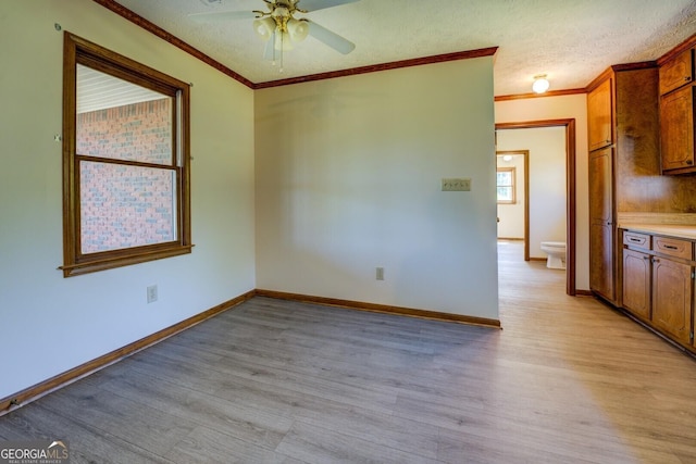 interior space featuring ceiling fan, ornamental molding, light wood-style floors, and a textured ceiling