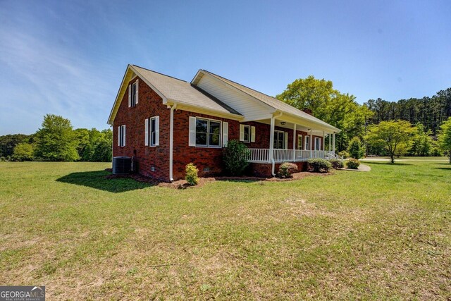 view of side of home with central AC unit, covered porch, brick siding, a yard, and crawl space