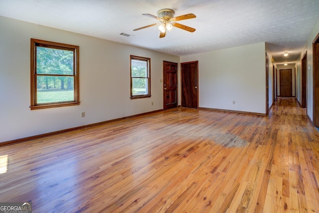 unfurnished room featuring baseboards, a ceiling fan, visible vents, and light wood-style flooring