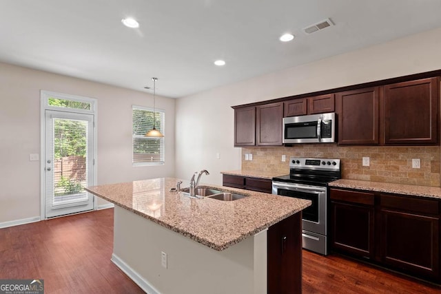 kitchen with stainless steel appliances, a sink, backsplash, a kitchen island with sink, and dark wood-type flooring