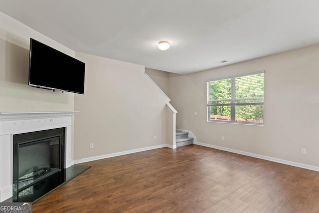 unfurnished living room with stairs, wood finished floors, baseboards, and a glass covered fireplace