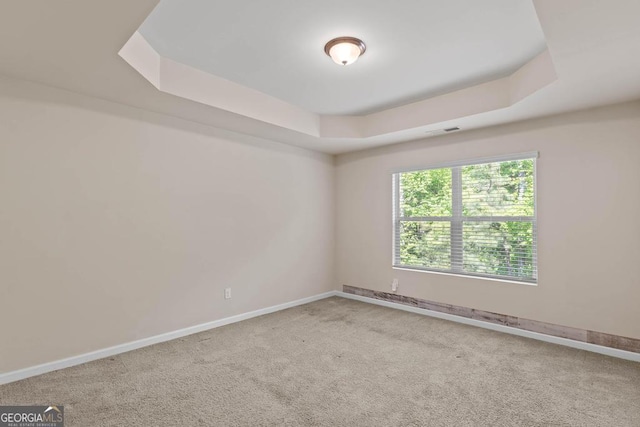 spare room with a tray ceiling, carpet, and baseboards