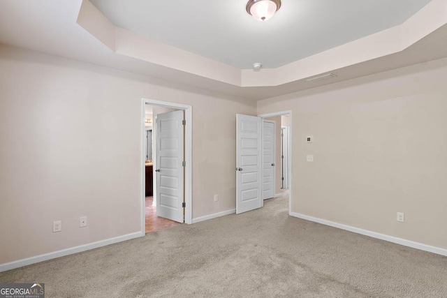 unfurnished bedroom featuring carpet, a raised ceiling, and baseboards