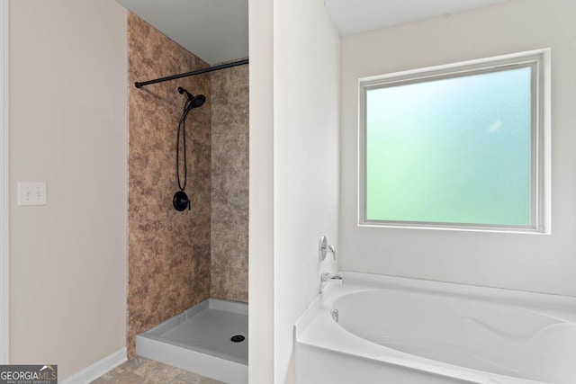 bathroom featuring a bath, a tile shower, and baseboards