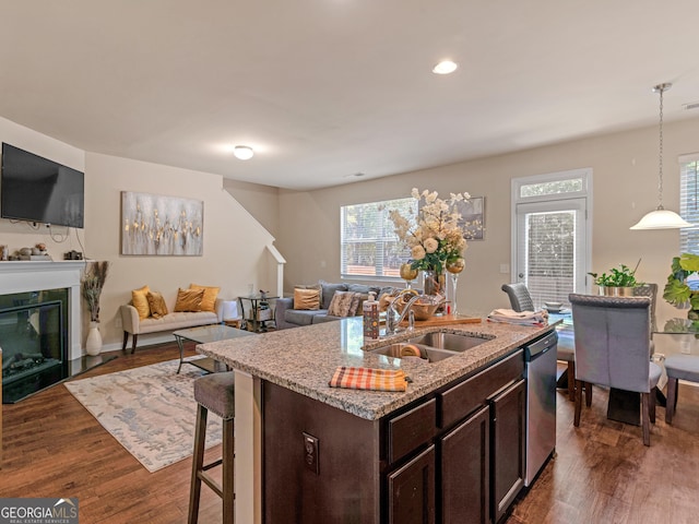 kitchen featuring a sink, dishwasher, dark brown cabinets, light stone counters, and healthy amount of natural light