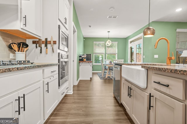 kitchen featuring white cabinets, stainless steel appliances, visible vents, backsplash, and wood finished floors
